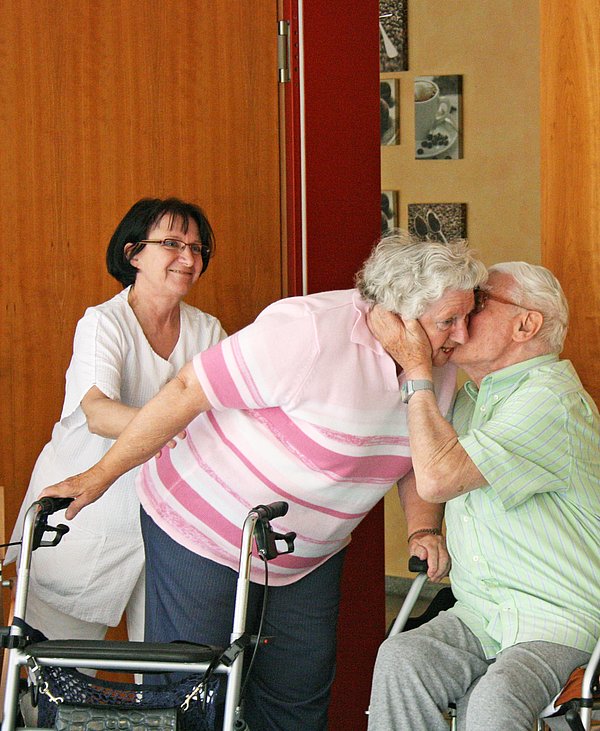 2 Bewohner begrüßen sich herzlich, im Hintergrund eine Mitarbeiterin