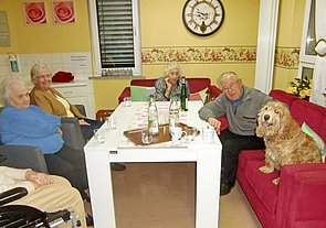 Bewohnerin in einem Gemeinschaftsraum am Tisch, mit dabei ist ein Hund